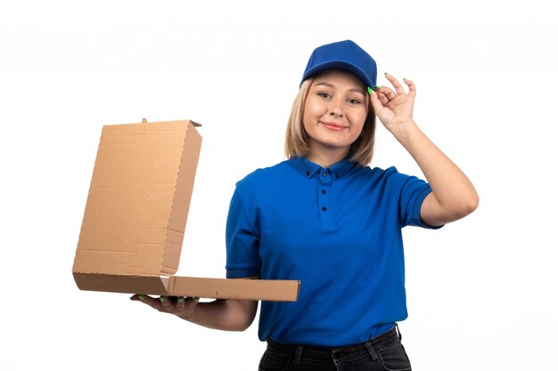 Una vista frontal joven mensajero en uniforme azul sosteniendo el paquete de entrega de alimentos con una sonrisa en su rostro