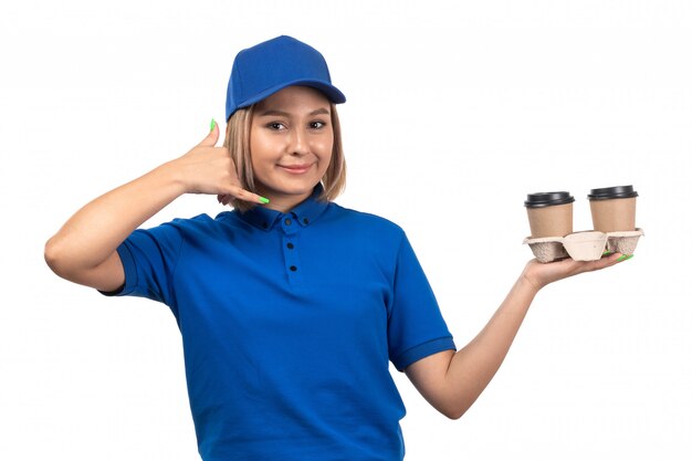 Una vista frontal joven mensajero en uniforme azul sosteniendo tazas de café