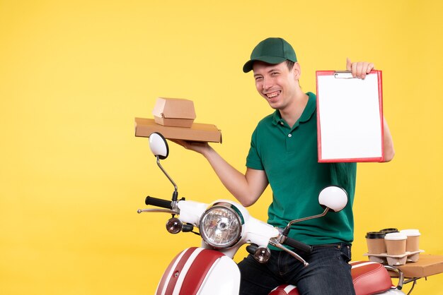 Vista frontal joven mensajero en uniforme sosteniendo cajas de comida y nota de archivo en amarillo