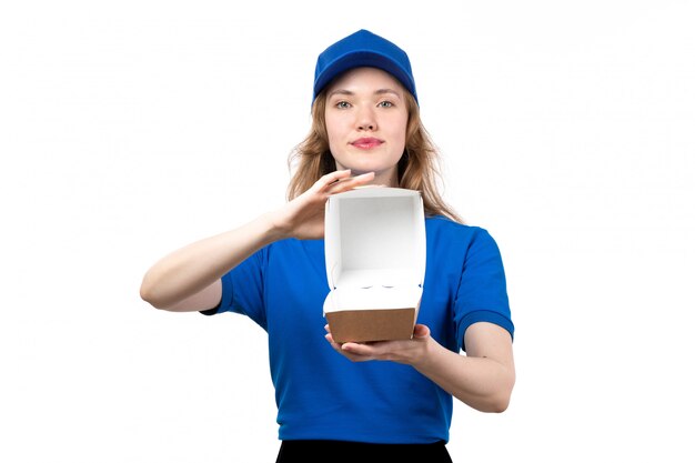 Una vista frontal joven mensajero en uniforme sosteniendo un paquete de entrega vacío sonriendo