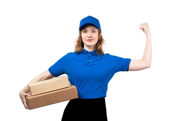 Una vista frontal joven mensajero en uniforme sosteniendo paquetes de entrega sonriendo y flexionando