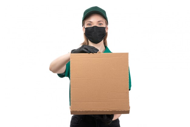 Una vista frontal joven mensajero en uniforme verde guantes negros y máscara negra con entrega de paquetes de comida