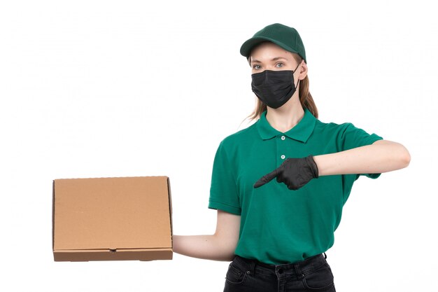 Una vista frontal joven mensajero en uniforme verde guantes negros y máscara negra con entrega de paquetes de comida