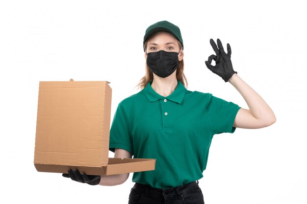 Una vista frontal joven mensajero en uniforme verde guantes negros y máscara negra con entrega de paquetes de comida