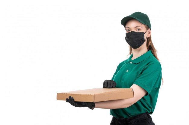 Una vista frontal joven mensajero en uniforme verde guantes negros y máscara negra con entrega de paquetes de comida