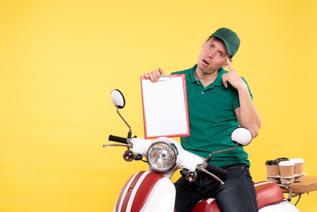 Vista frontal joven mensajero en uniforme verde con nota de archivo en amarillo