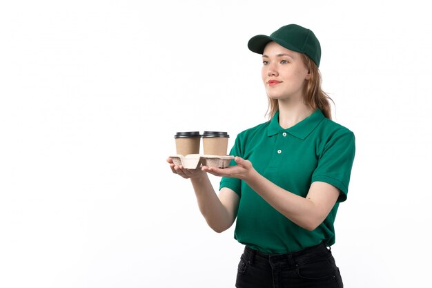 Una vista frontal joven mensajero en uniforme verde sonriendo entregando tazas de café