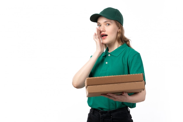 Una vista frontal joven mensajero en uniforme verde sonriendo sosteniendo paquetes con comida susurrando