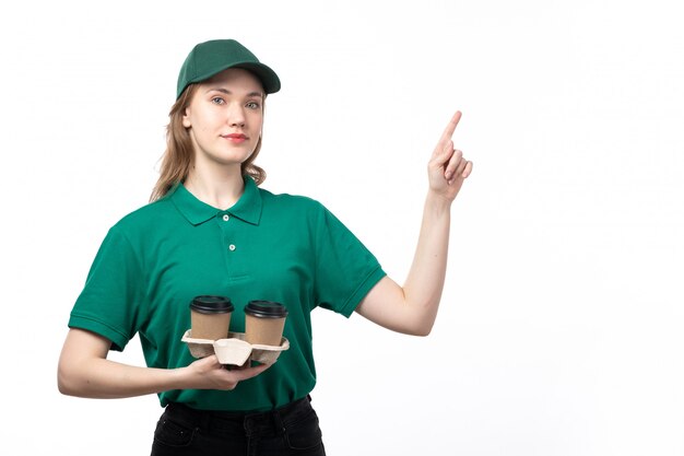 Una vista frontal joven mensajero en uniforme verde sosteniendo tazas de café sonriendo