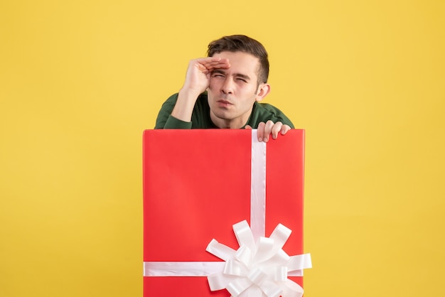 Foto gratuita vista frontal joven mirando algo parado detrás de caja de regalo grande en amarillo