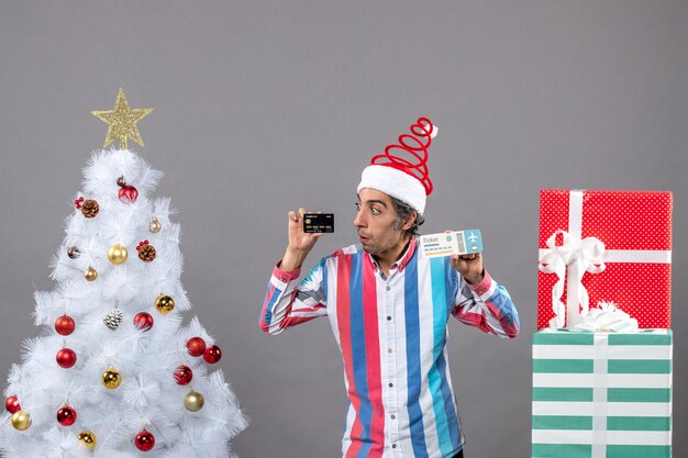 Vista frontal joven mirando la tarjeta alrededor del árbol de Navidad