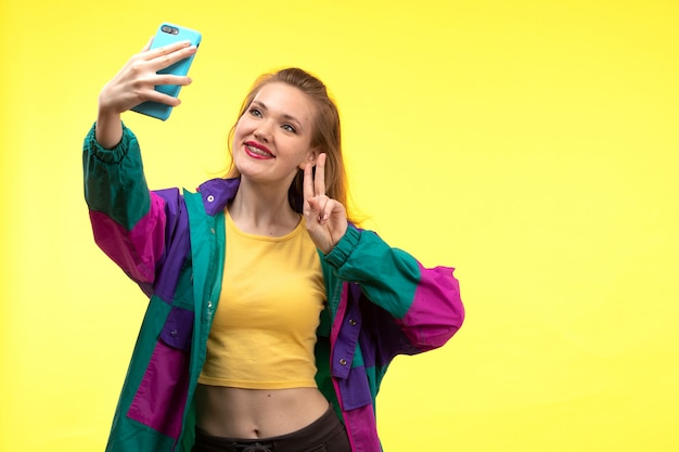 Foto gratuita una vista frontal joven moderna en camisa amarilla pantalón negro y chaqueta colorida tomando una selfie en el teléfono feliz expresión