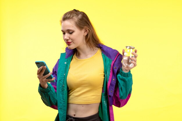 Una vista frontal joven moderna en camisa amarilla pantalón negro y chaqueta colorida usando su teléfono