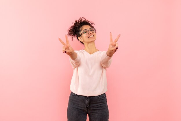 Vista frontal de la joven mostrando el número con una sonrisa en la pared rosa