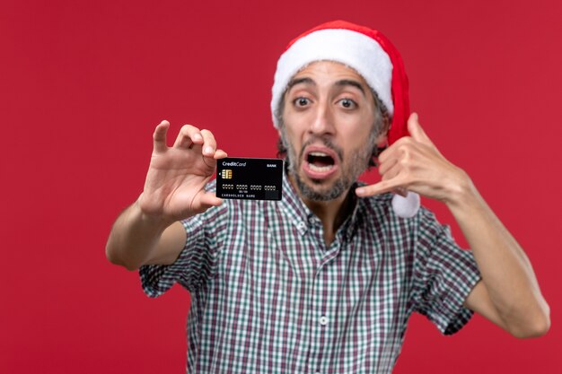 Vista frontal joven mostrando tarjeta bancaria sobre fondo rojo.