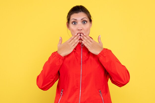 Vista frontal joven mujer en abrigo rojo sorprendido sobre fondo amarillo