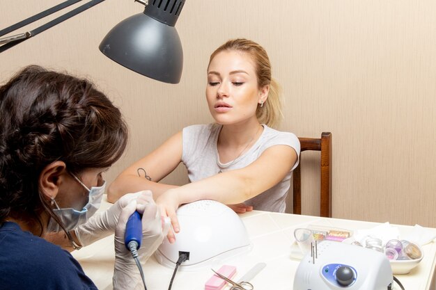 Vista frontal joven mujer arreglando sus uñas por manicurista dentro de la habitación belleza mujer manicura autocuidado de uñas