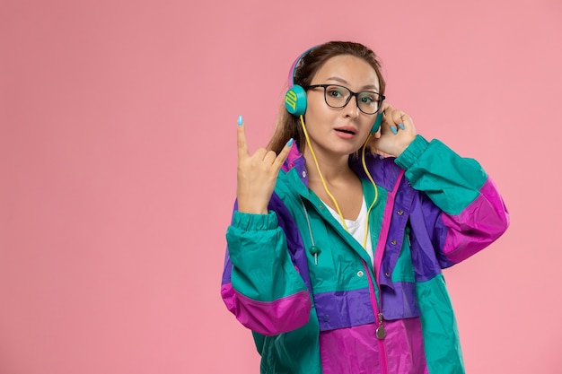 Foto gratuita vista frontal joven mujer atractiva en abrigo de color camiseta blanca escuchando música sobre fondo rosa