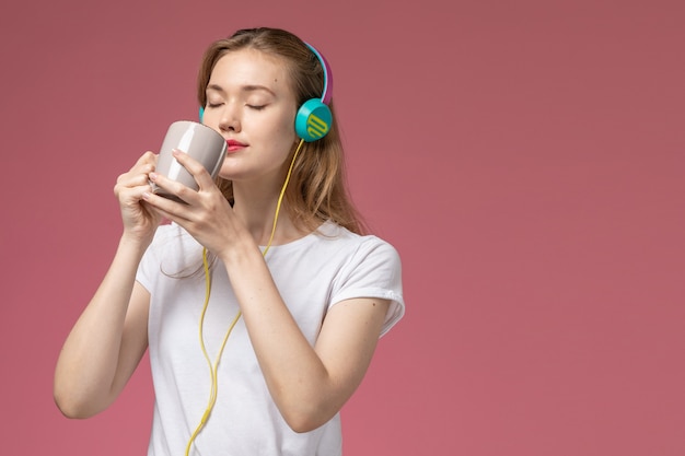 Vista frontal joven mujer atractiva bebiendo té y escuchando música en la pared rosa modelo color mujer joven