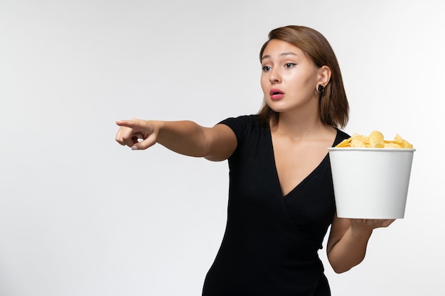 Vista frontal joven mujer atractiva en camisa negra con patatas fritas viendo la película en la superficie blanca