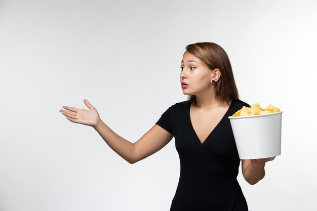 Vista frontal joven mujer atractiva en camisa negra con patatas fritas viendo la película en la superficie blanca