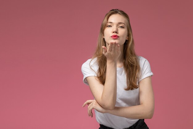 Vista frontal joven mujer atractiva en camiseta blanca enviando besos al aire en la pared rosa modelo pose femenina foto en color