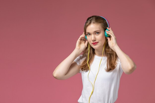 Vista frontal joven mujer atractiva en camiseta blanca escuchando música con una sonrisa en el modelo de escritorio rosa oscuro color mujer joven