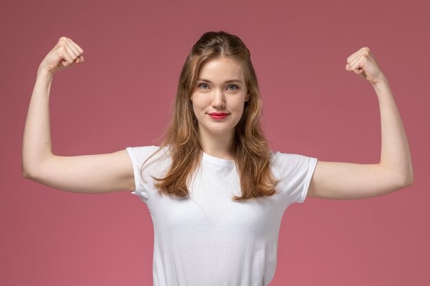 Vista frontal joven mujer atractiva en camiseta blanca flexionando sobre rosa modelo de escritorio color mujer joven