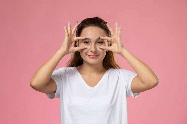 Vista frontal joven mujer atractiva en camiseta blanca posando y smi sobre fondo rosa