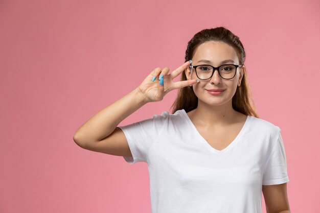 Vista frontal joven mujer atractiva en camiseta blanca smi posando sobre fondo rosa