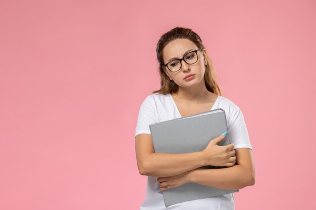 Vista frontal joven mujer atractiva en camiseta blanca sosteniendo archivos grises y pensando en el fondo rosa