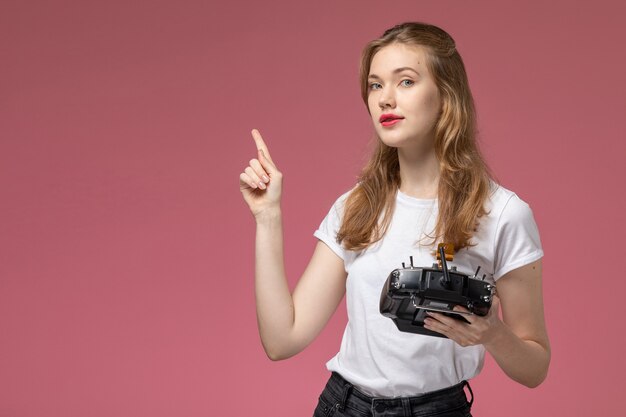 Vista frontal joven mujer atractiva en camiseta blanca sosteniendo el mando a distancia en la pared rosa modelo color hembra joven