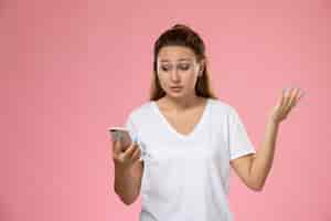 Foto gratuita vista frontal joven mujer atractiva en camiseta blanca con su teléfono sobre fondo rosa