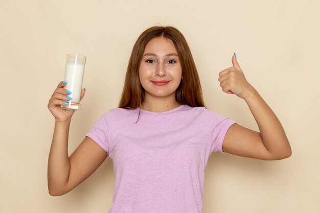 Vista frontal joven mujer atractiva en camiseta rosa y jeans bebiendo leche fría fresca