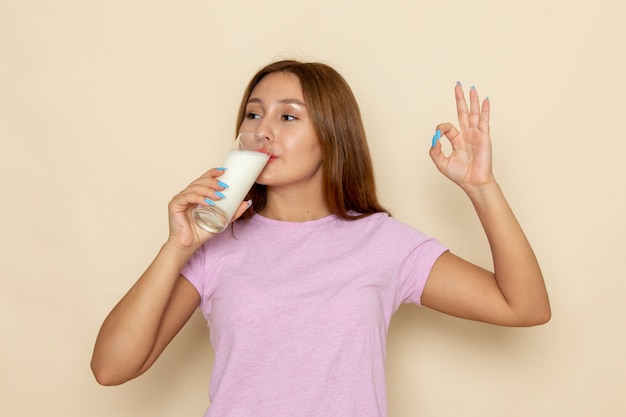 Vista frontal joven mujer atractiva en camiseta rosa y jeans bebiendo leche