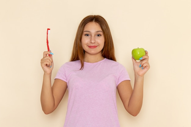 Vista frontal joven mujer atractiva en camiseta rosa y jeans con manzana y cepillo de dientes