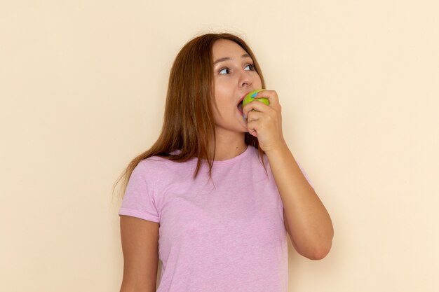 Vista frontal joven mujer atractiva en camiseta rosa y jeans mordiendo manzana verde