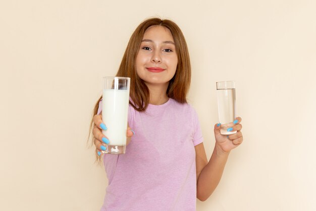 Vista frontal joven mujer atractiva en camiseta rosa y jeans sosteniendo leche y agua con sonrisa