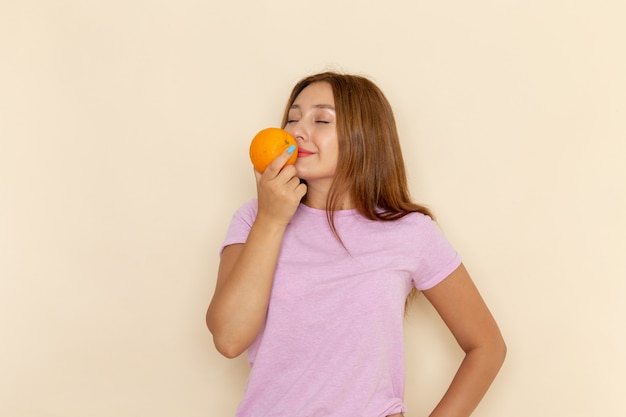 Vista frontal joven mujer atractiva en camiseta rosa y jeans sosteniendo naranja y oliendo