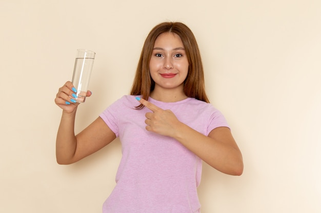 Vista frontal joven mujer atractiva en camiseta rosa y jeans sosteniendo un vaso de agua con una sonrisa