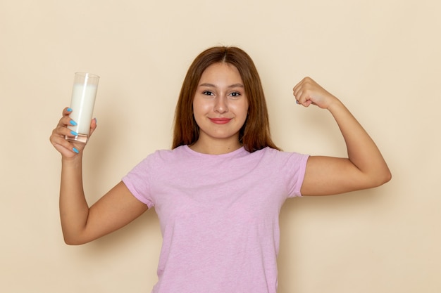 Vista frontal joven mujer atractiva en camiseta rosa y jeans sosteniendo un vaso de leche y flexionando