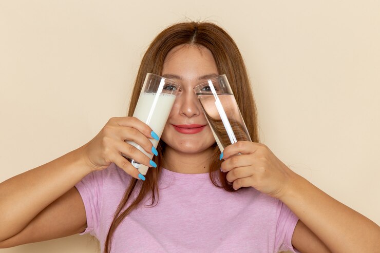 Vista frontal joven mujer atractiva en camiseta rosa y jeans sosteniendo vasos de agua y leche
