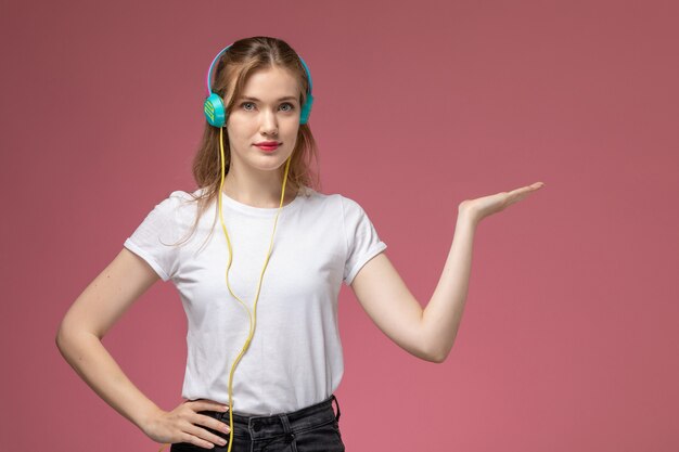 Foto gratuita vista frontal joven mujer atractiva escuchando música con auriculares en la pared de color rosa oscuro modelo color mujer joven