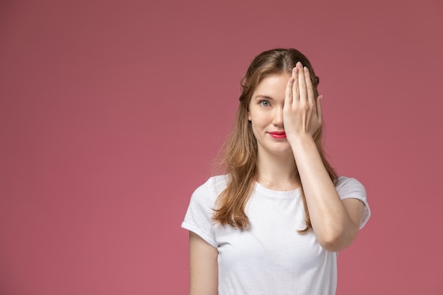 Vista frontal joven mujer atractiva sonriendo cubriendo la mitad de su rostro en la pared rosa modelo color mujer joven