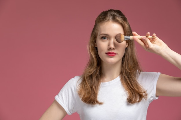 Vista frontal joven mujer atractiva sosteniendo pincel de maquillaje en la pared rosa modelo color mujer joven