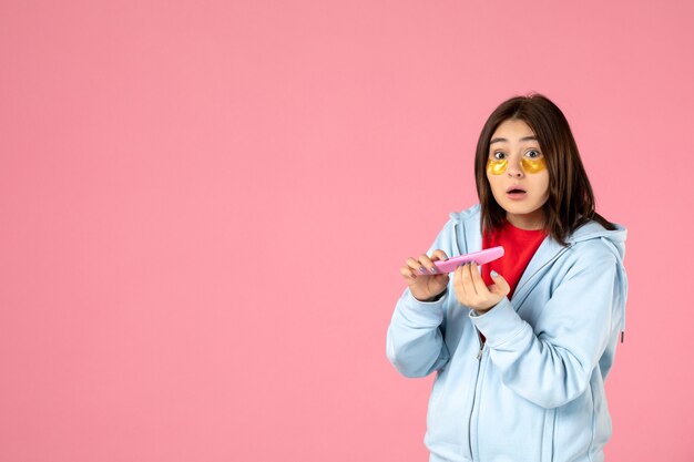 Vista frontal joven mujer bonita con parches en los ojos y lima de uñas sobre fondo rosa