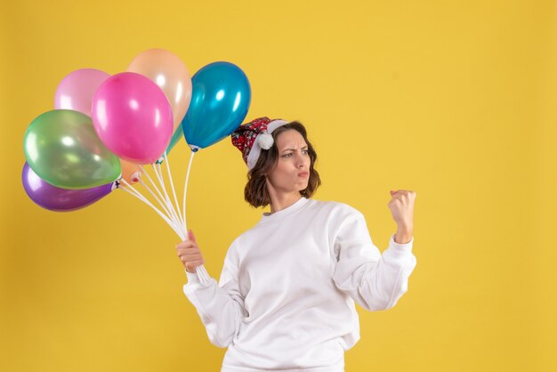 Vista frontal joven mujer bonita sosteniendo globos en color amarillo navidad año nuevo emoción mujer