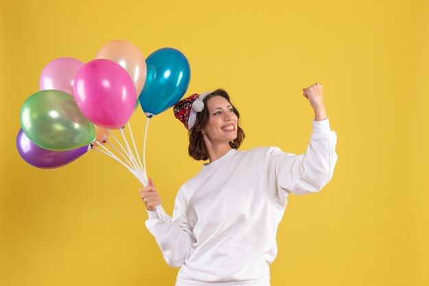 Vista frontal joven mujer bonita sosteniendo globos en color amarillo navidad año nuevo emoción mujer