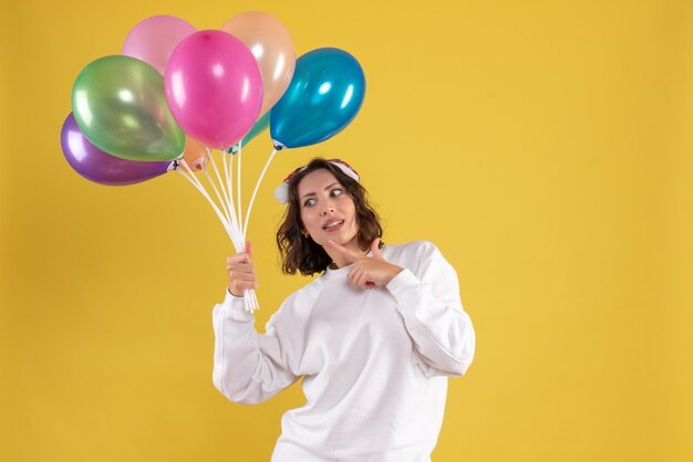 Vista frontal joven mujer bonita sosteniendo globos en el escritorio amarillo mujer de navidad año nuevo color emoción