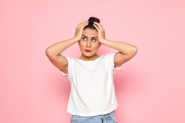 Una vista frontal joven mujer en camiseta blanca y jeans azul posando con expresión confusa